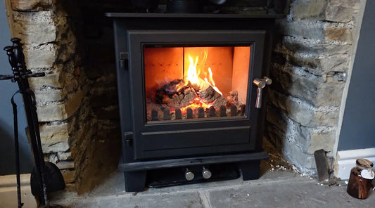 Una moderna stufa a legna in ghisa nera incassata in un caminetto di pietra rustica, con fiamme vivaci che bruciano tronchetti di legno ad alta efficienza.